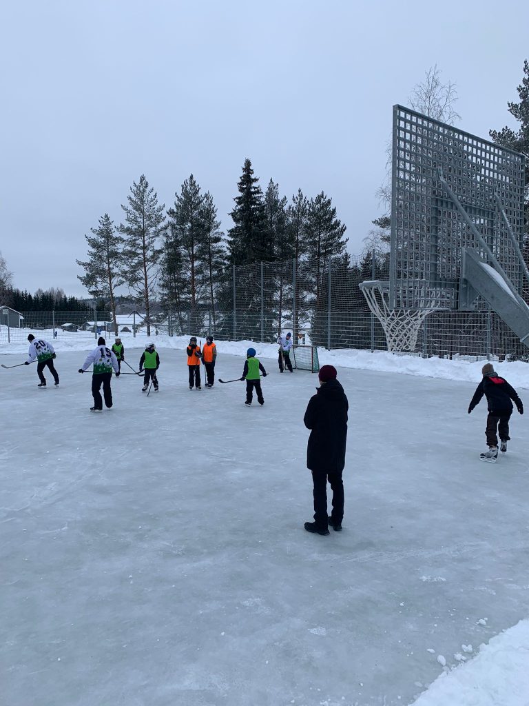 Lapsia ja aikuisia pelaamassa jääpalloa Virenojan koulun kentällä
