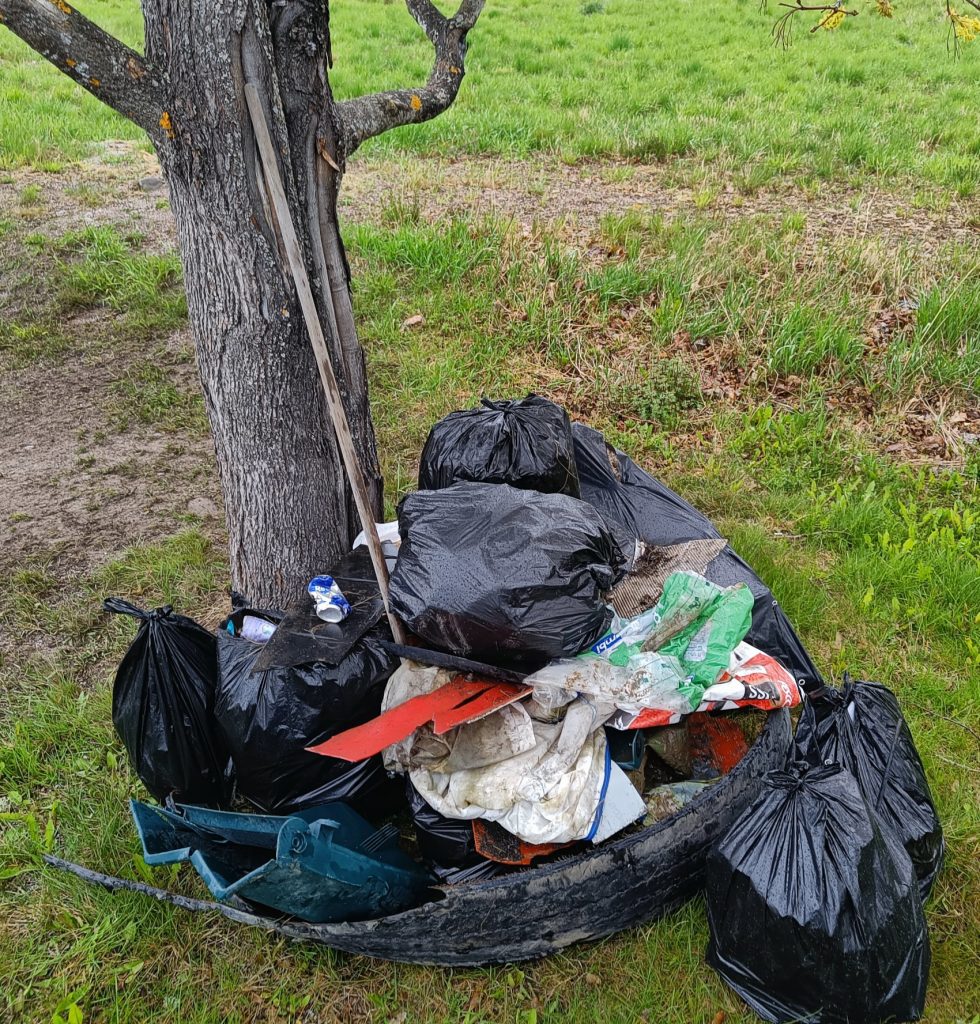 Puun edustalla on kasa jätesäkkejä, joiden päälle on heitetty irrallaan olevia isompia roskia odottamaan roska-autoa.