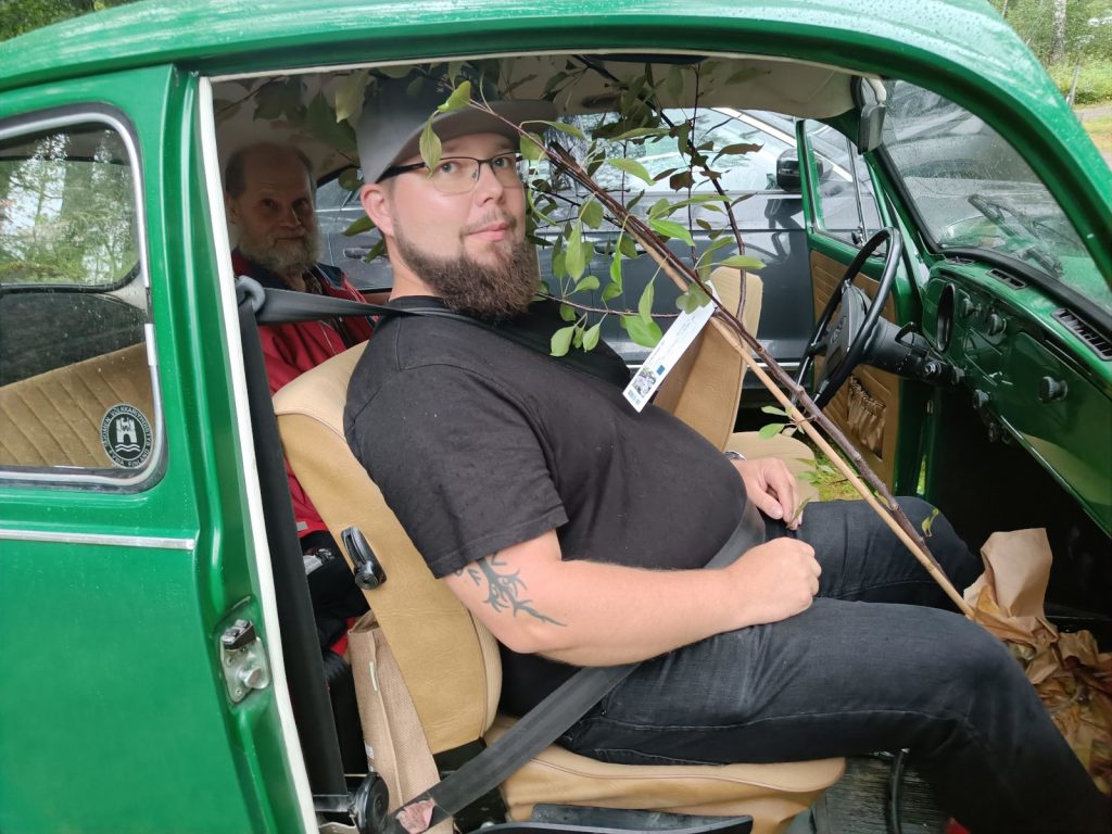 Vanhan kuplavolkkarin etumatkustajalla on jalkatilassaan omenapuun taimen ruukku. Varsi ulottuu auton kattoa pitkin viistosti takapenkille saakka.